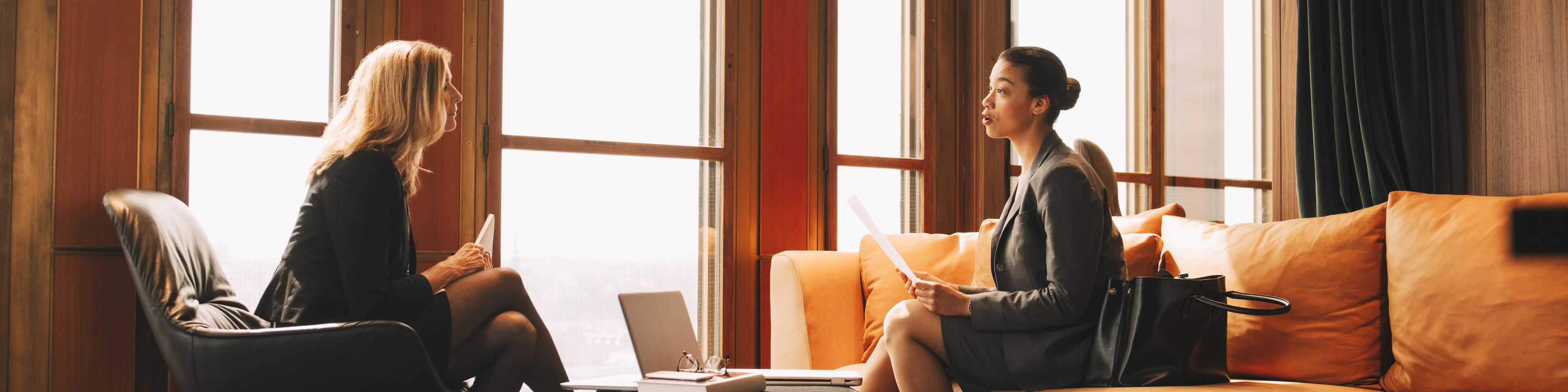 Full length of female lawyers discussing while sitting by window at office